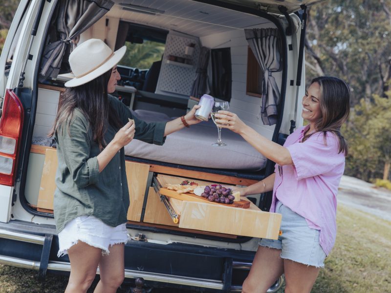 Two girls using the campervan and having some nibbles and a drink